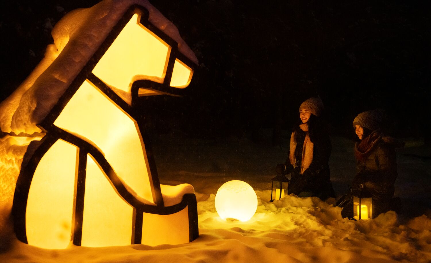 Two girls sit in front of a light-up polar bear at In Search of Christmas Spirit in Banff National Park.